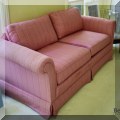 F33. Pink upholstered sofa on casters. 27”h x 78”w x 34”d 